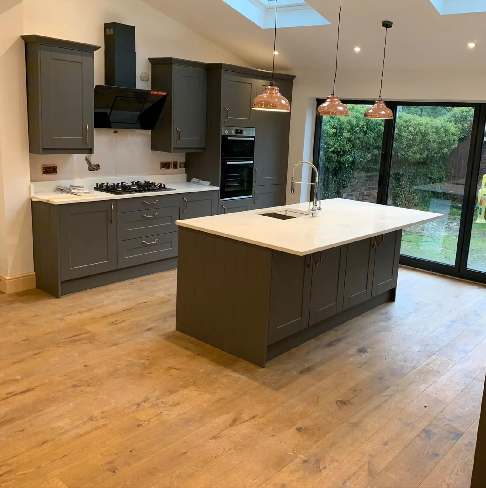 New grey shaker kitchen with a white-topped island and bi-fold doors to the garden