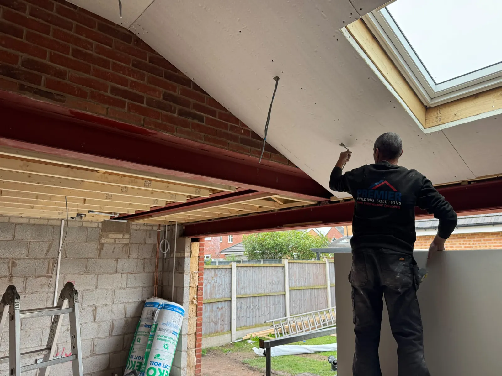 Builder fitting ceiling boards beneath extension roof framing
