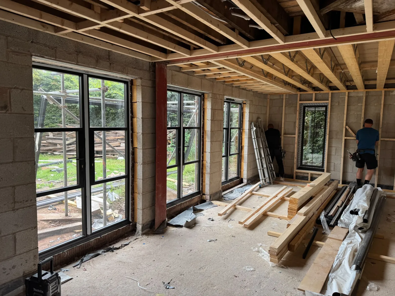 Extension interior under construction with new floor joists and black framed glazing