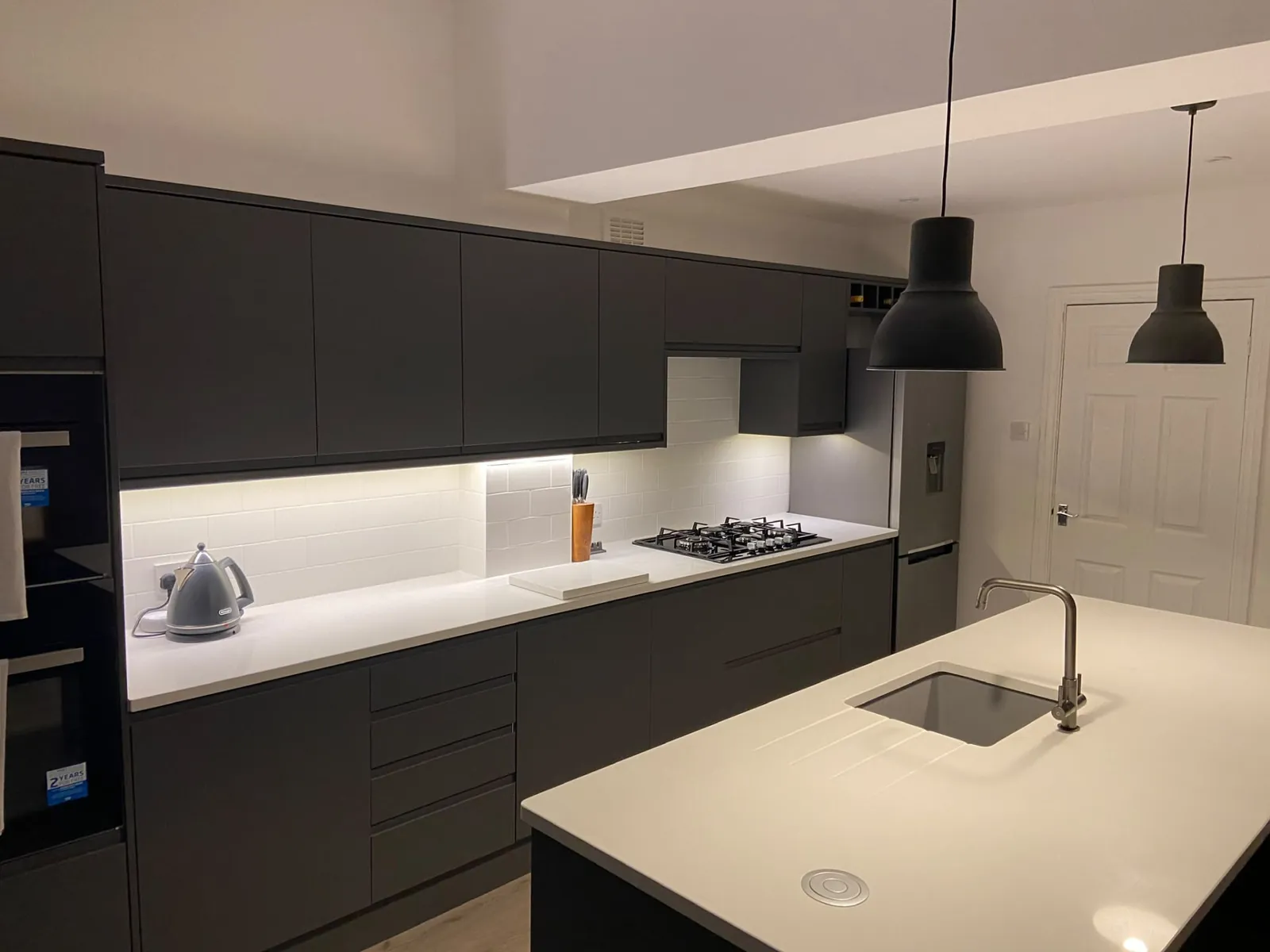 Fitted dark grey kitchen with white worktops, tiled splashback and island sink