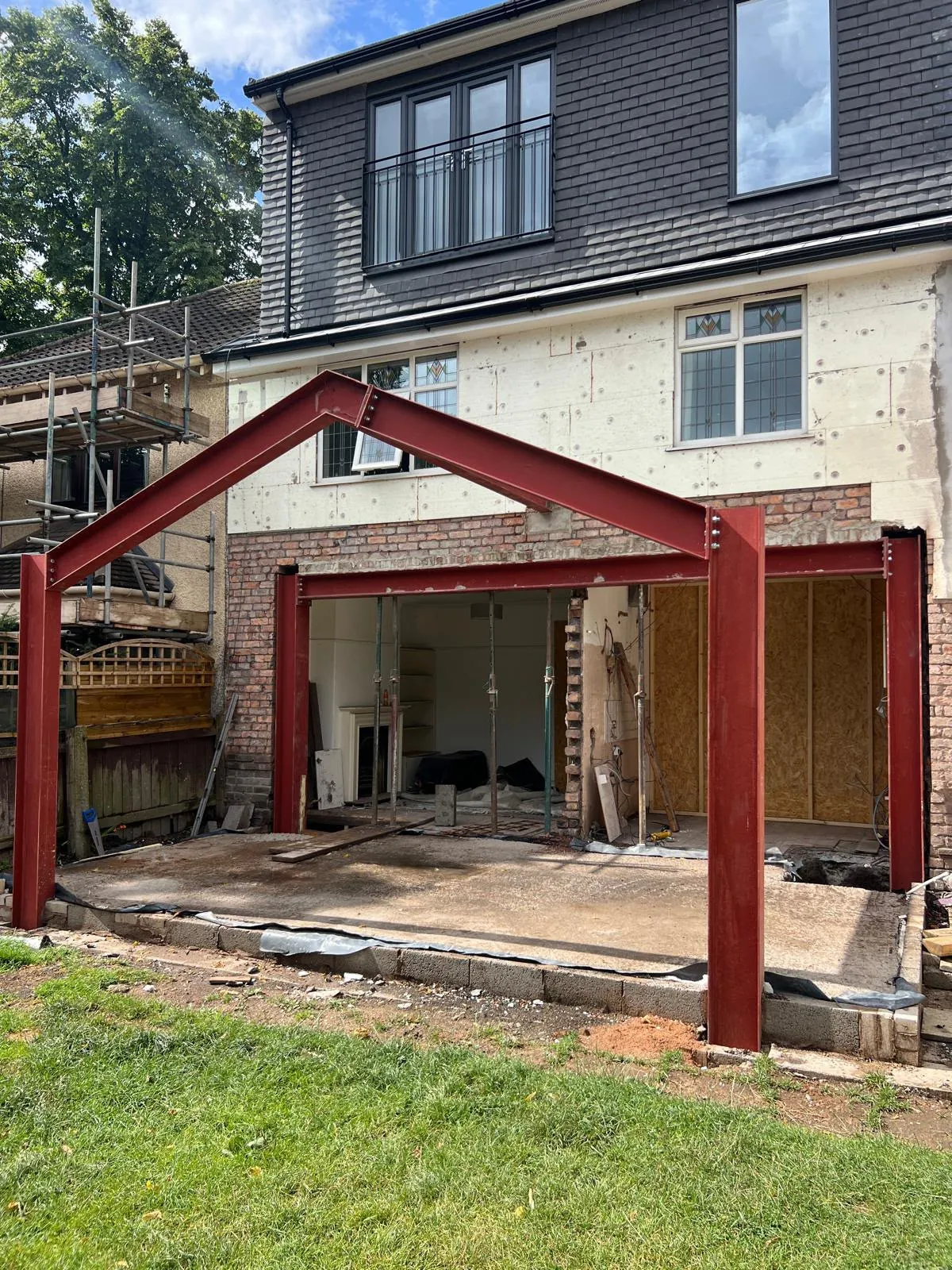 Red structural steel frame and brickwork for a house extension with scaffolding