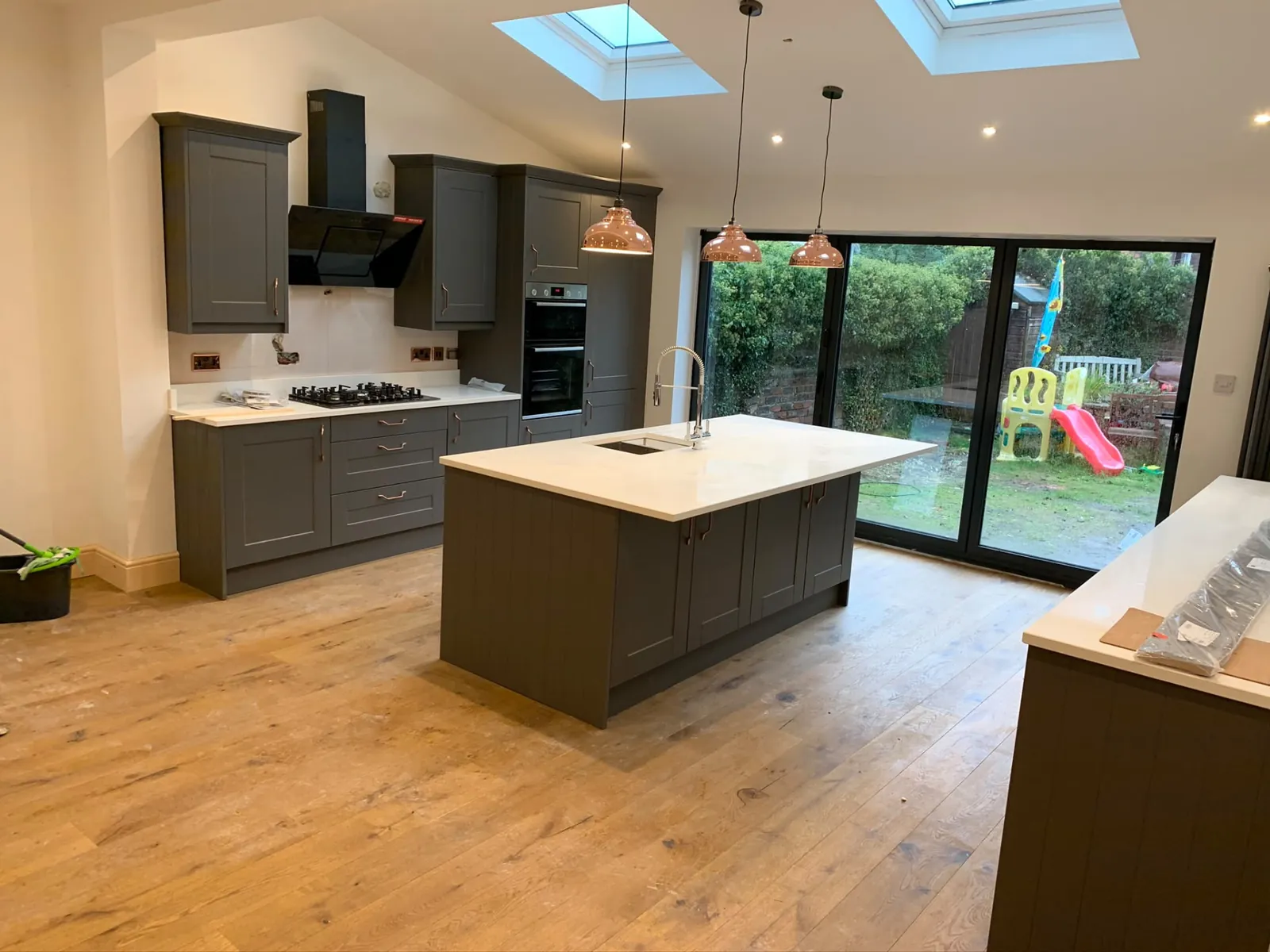 Grey shaker kitchen with island, copper pendants and bi-fold doors to the garden
